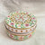 Decorative round box with floral patterns on a white fabric background