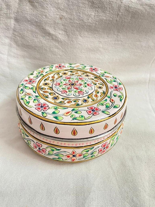 Decorative round box with floral patterns on a white fabric background