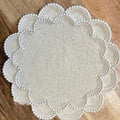Round pearl-beaded white placemat with intricate concentric patterns and scalloped edges, placed on a wooden surface.