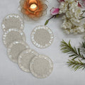 Set of round beaded coasters on a light surface with flowers and a candle in the background.