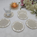 Set of round beaded coasters on a light surface with a glass, candle, and flowers.
