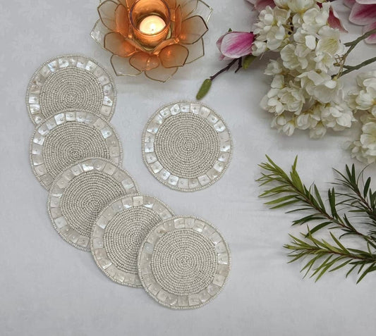 Set of round beaded coasters on a light surface with flowers and a candle in the background.