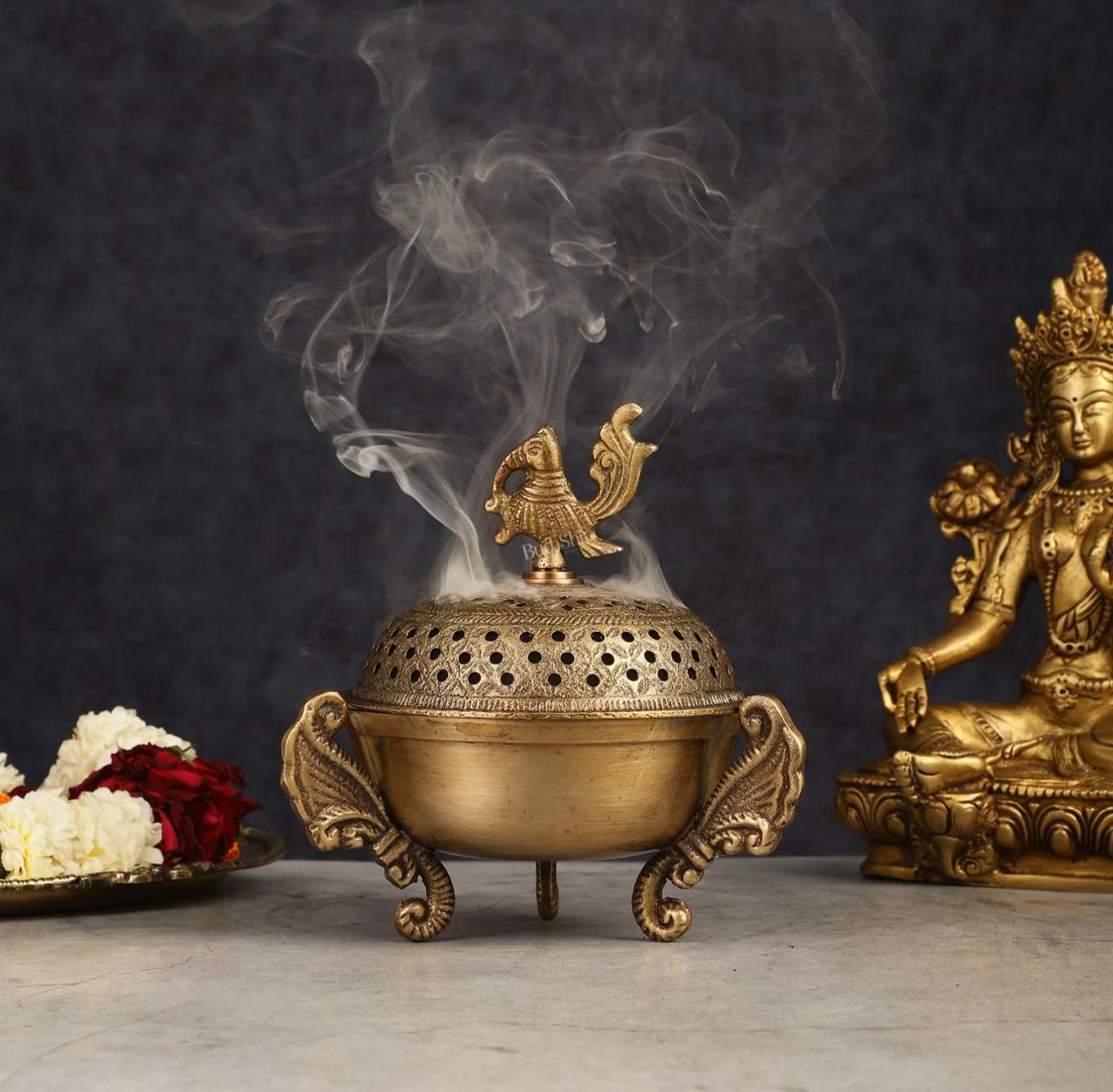 Bronze incense burner with smoke, flowers, and a statue on a dark background