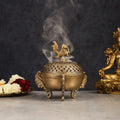 Bronze incense burner with smoke, flowers, and statue on a dark background