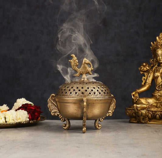 Bronze incense burner with smoke, flowers, and statue on a dark background