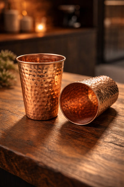 Two copper tumblers on a wooden surface with a blurred background