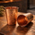 Two copper tumblers on a wooden surface with a blurred background