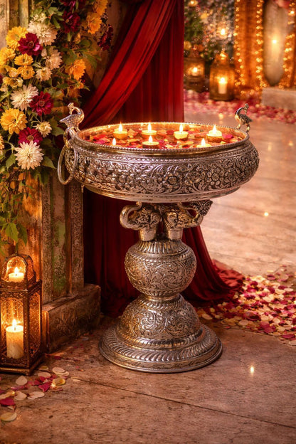 Decorative metal bowl with floating candles on a wooden floor with flowers and red fabric in the background