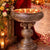 Decorative metal bowl with floating candles on a wooden floor with flowers and red fabric in the background