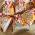 Decorative bags with pink, orange, and beige colors and silver embellishments on a beige fabric background.