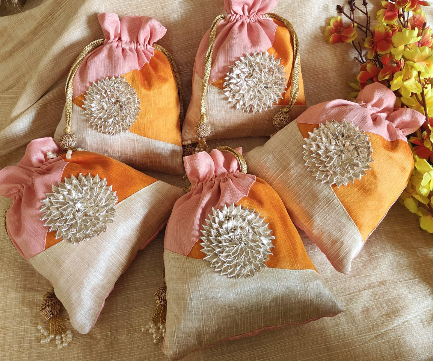 Decorative bags with pink, orange, and beige colors and silver embellishments on a beige fabric background.