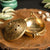 Brass incense burner with intricate designs on a wooden surface with plants in the background