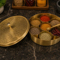 Brass spice container with various spices on a dark surface