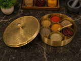 Brass spice container with various spices on a dark surface