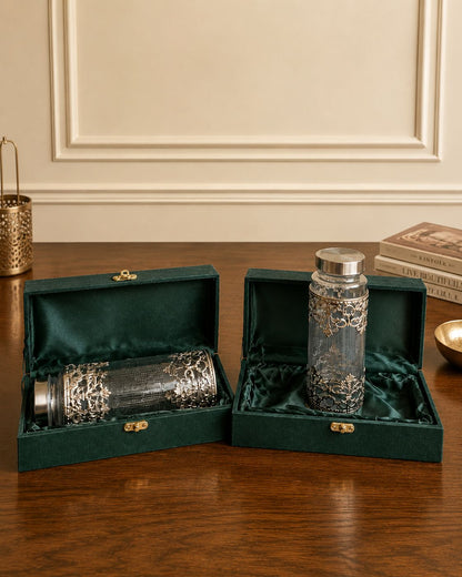 Two glass bottles with silver caps in green velvet boxes on a wooden surface.