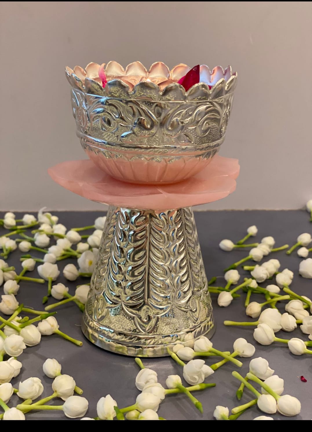 Decorative silver bowl on a pink stand with white flowers on a gray surface