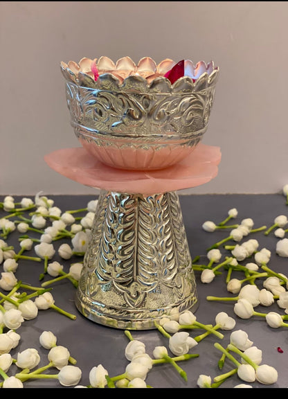 Decorative silver bowl on a pink stand with white flowers on a gray surface