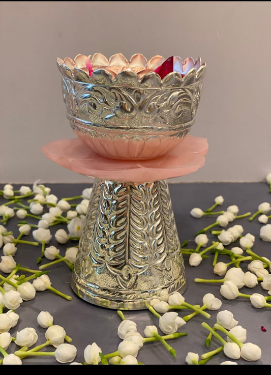 Decorative silver bowl on a pink stand with white flowers on a gray surface