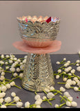 Decorative silver bowl on a pink stand with white flowers on a gray surface