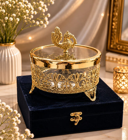 Decorative gold bowl with intricate designs on a black base, surrounded by flowers and a candle.