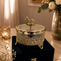 Decorative gold jewelry box on a black stand with flowers and candles in the background