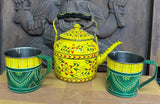 Decorative yellow teapot with floral patterns and matching cups on a wooden surface.