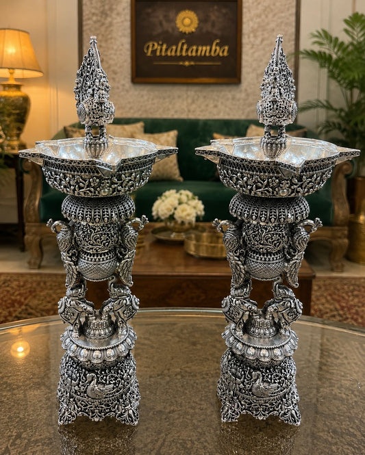 Decorative silver candle holders on a reflective surface with a blurred background