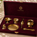 Pitaltamba brass and gold-toned ceremonial set displayed inside an open deep burgundy velvet gift box, with the brand name printed in gold on the inside lid.
