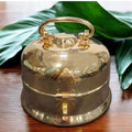 Gold bell on a wooden surface with green leaves in the background