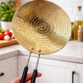 Gold frying pan with black handles held in a kitchen