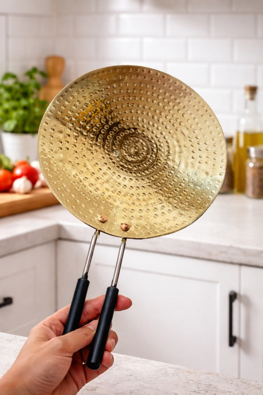 Gold frying pan with black handles held in a kitchen