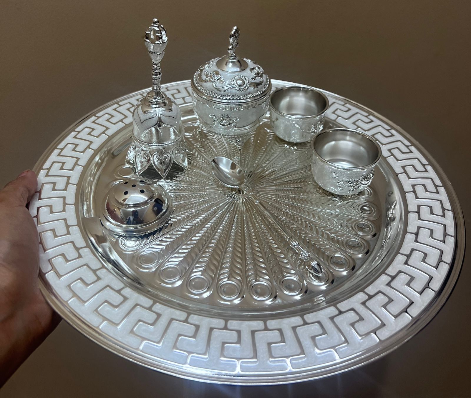 Decorative silver tray with intricate designs and small containers on a brown background