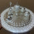 Decorative silver tray with intricate designs and small containers on a brown background