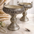 Two ornate silver bowls on a marble surface with a soft curtain background