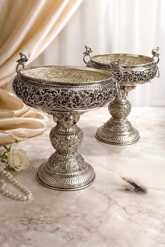 Two ornate silver bowls on a marble surface with a soft curtain background