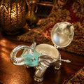 Silver elephant-shaped container with a green gem on a wooden surface