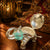 Silver elephant-shaped container with a green gem on a wooden surface