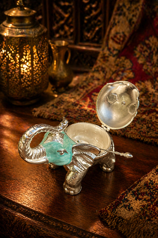 Silver elephant-shaped container with a green gem on a wooden surface
