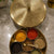 Decorative brass spice holder with various spices on a marble surface