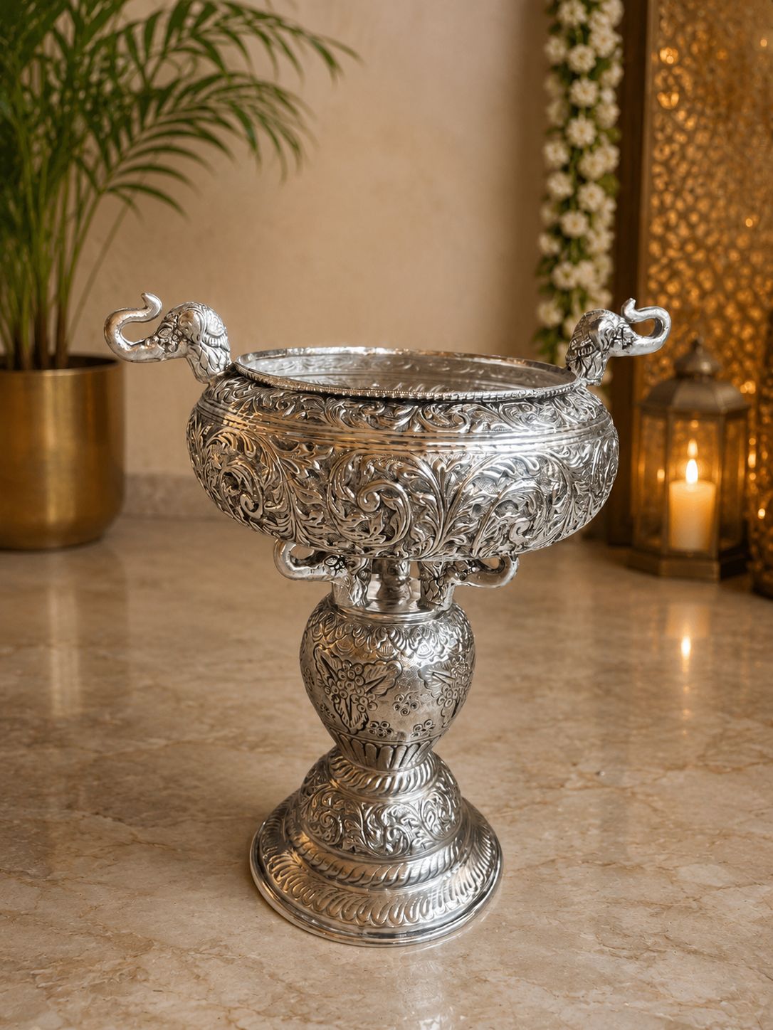 Decorative silver urn on a marble surface with a plant and candle in the background