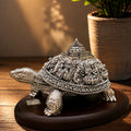 Decorative silver turtle figurine on a wooden surface with a potted plant in the background