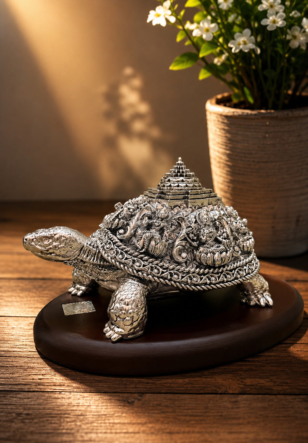 Decorative silver turtle figurine on a wooden surface with a potted plant in the background