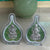 Two silver figurines in clear plastic cases on a light surface with a green pot in the background.