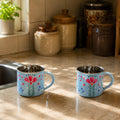 Two floral mugs on a kitchen counter with jars and a plant in the background.