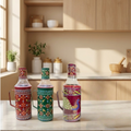 Three decorative bottles on a kitchen counter with wooden cabinets and shelves in the background.
