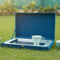 Tea set with three cups and a tray in an open blue box on grass