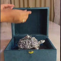 Decorative silver turtle figurine placed on a polished wooden base with a soft green background, symbolizing prosperity and elegance.