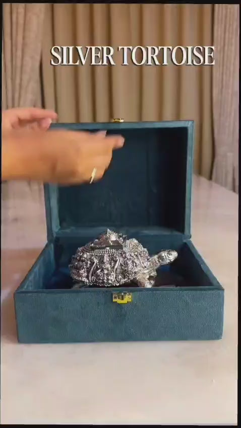 Decorative silver turtle figurine placed on a polished wooden base with a soft green background, symbolizing prosperity and elegance.
